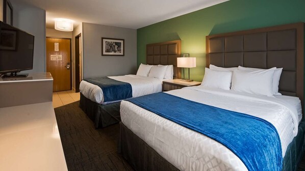 A hotel room with two beds, a television, a painting on the wall, and a door.