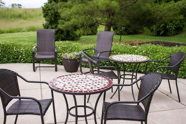 An outdoor patio with four wicker chairs and two round tables with mosaic tops, surrounded by greenery. - Baymont by Wyndham Maumee Toledo (Maumee)
