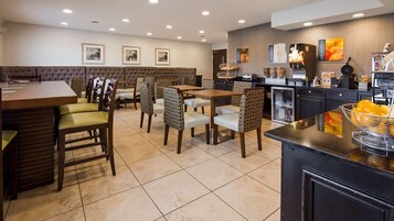 Un comedor de hotel con una larga mesa, sillas, un banco acolchado y una encimera de cocina con electrodomésticos.
