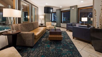 Un moderno vestíbulo de hotel con un sofá de cuero marrón, un sillón azul y una alfombra estampada.