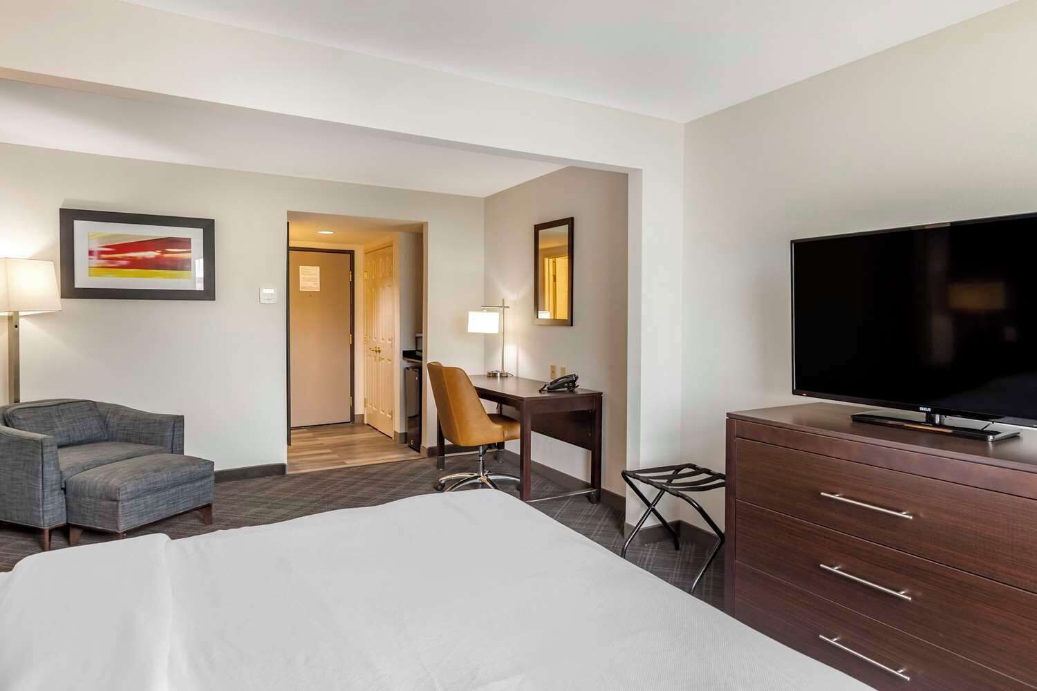 A hotel room with a bed, a desk, a chair, a television, and artwork on the walls.