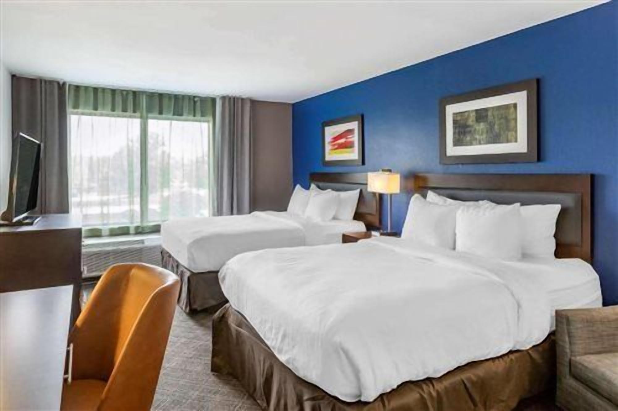 A hotel room with two beds, a desk, and a chair.