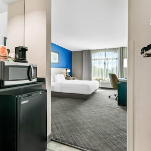 Een hotelkamer met een bed, een bureau met een computer, een magnetron en een koffiezetapparaat.