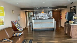 A hotel lobby with a reception desk, a brown leather sofa, a striped rug, and a wooden floor. - Days Inn by Wyndham Wauseon (Wauseon)