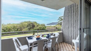 A balcony with a table set for two, overlooking a scenic landscape with trees and a distant hill. - Ocean Shores, 5 27 Weatherly Close - waterfront unit with views to Shoal Bay and wifi (Nelson Bay)