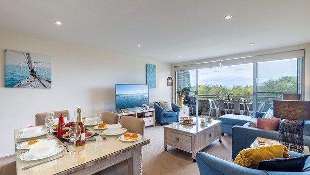 A modern living room with a dining area, a television, and a balcony with outdoor seating. - Ocean Shores, 5 27 Weatherly Close - waterfront unit with views to Shoal Bay and wifi (Nelson Bay)