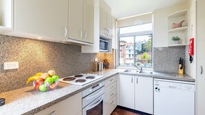 A modern kitchen with granite countertops, white cabinets, a built-in microwave, and a window with a view of buildings. - Ocean Shores, 5 27 Weatherly Close - waterfront unit with views to Shoal Bay and wifi (Nelson Bay)