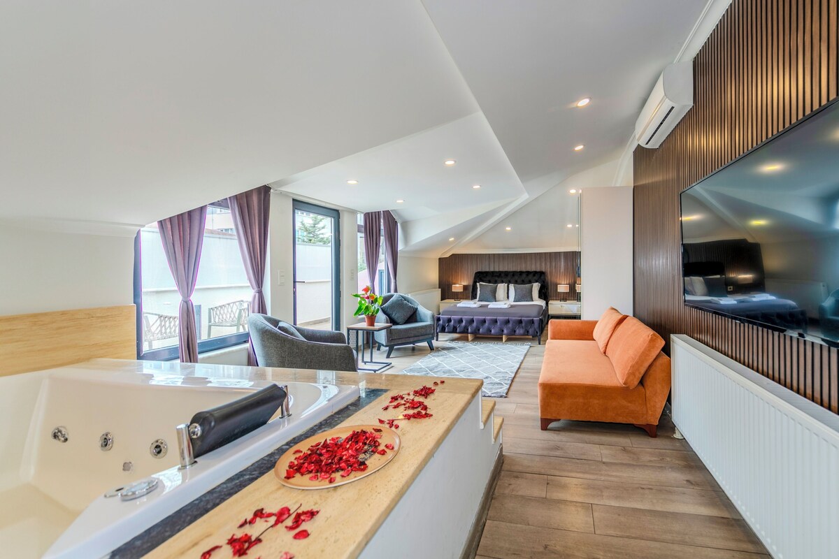 A modern hotel room with a large bed, a sofa, a TV, and a bathroom with a bathtub.