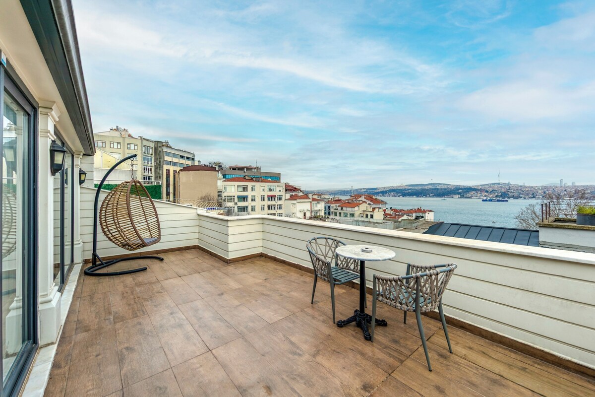 A balcony with a view of a river, a table with chairs, and a hanging chair.