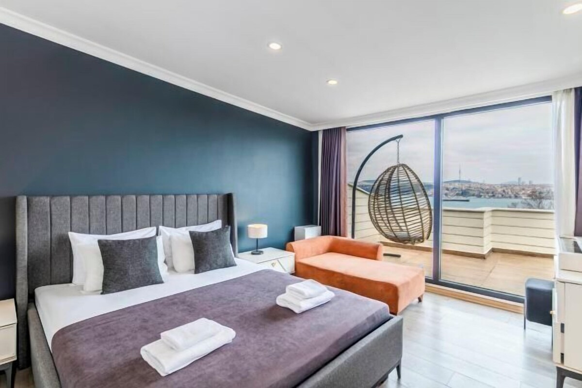 A modern hotel room with a large bed, a seating area, and a balcony with a city view.