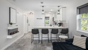 Ett modernt kök med en central köksö, barstolar och en svart soffa med randiga kuddar.