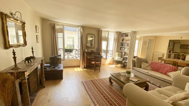 A living room with a sofa, a coffee table, a TV, a bookshelf, and a dining area with a table and chairs. - RIVE GAUCHE - RIVOLI/LOUVRE Type 3/4 approx. 100m2 in absolute calm (Paris)