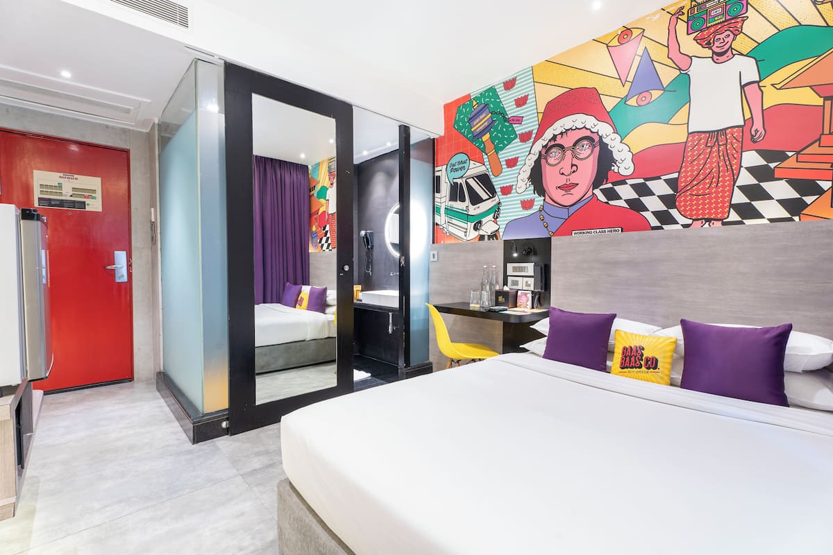 Ein Hotelzimmer mit Bett, Schreibtisch, Stuhl, Bad und einem farbenfrohen Wandgemälde.