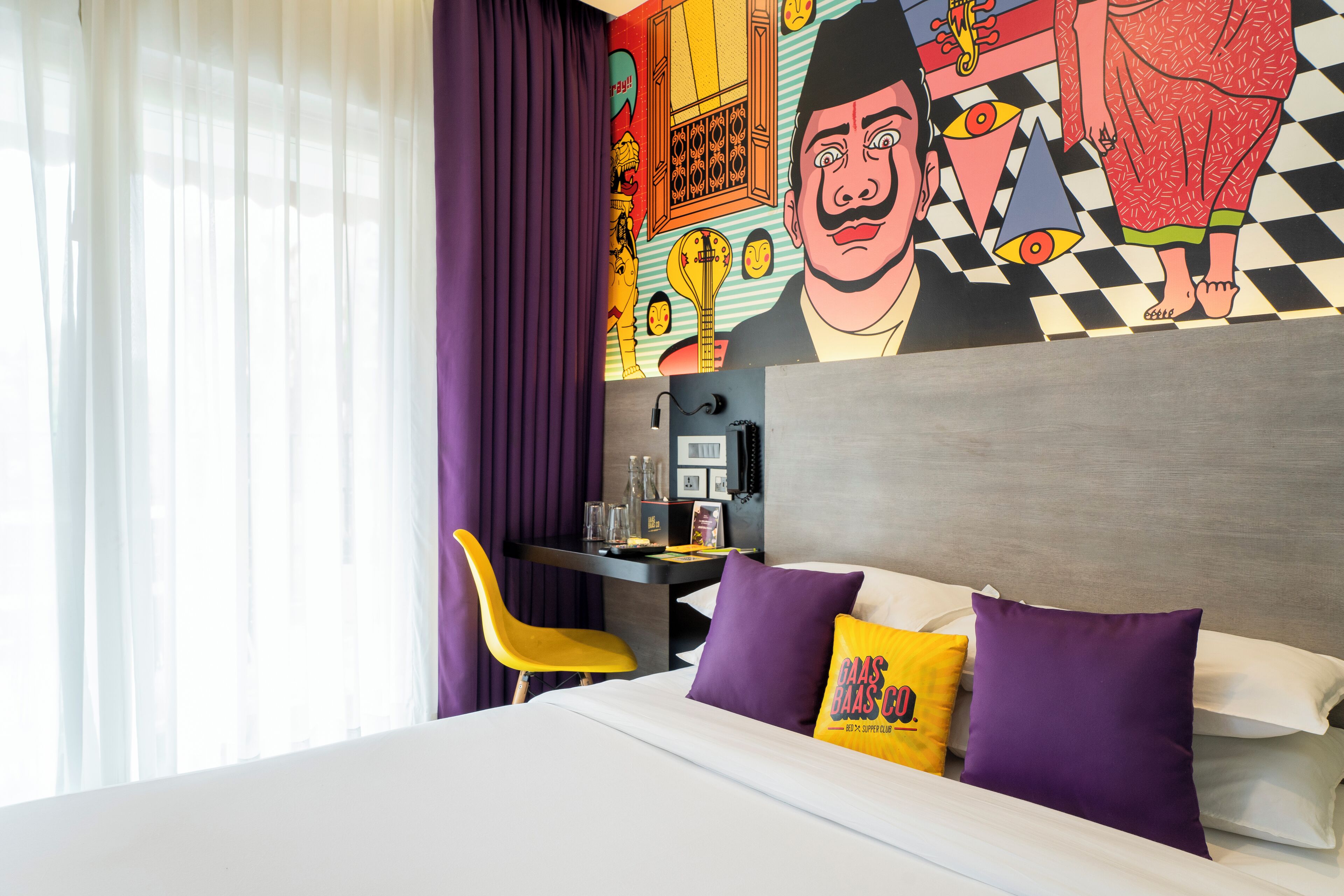 A hotel room with a bed, a desk, and a vibrant mural on the wall.