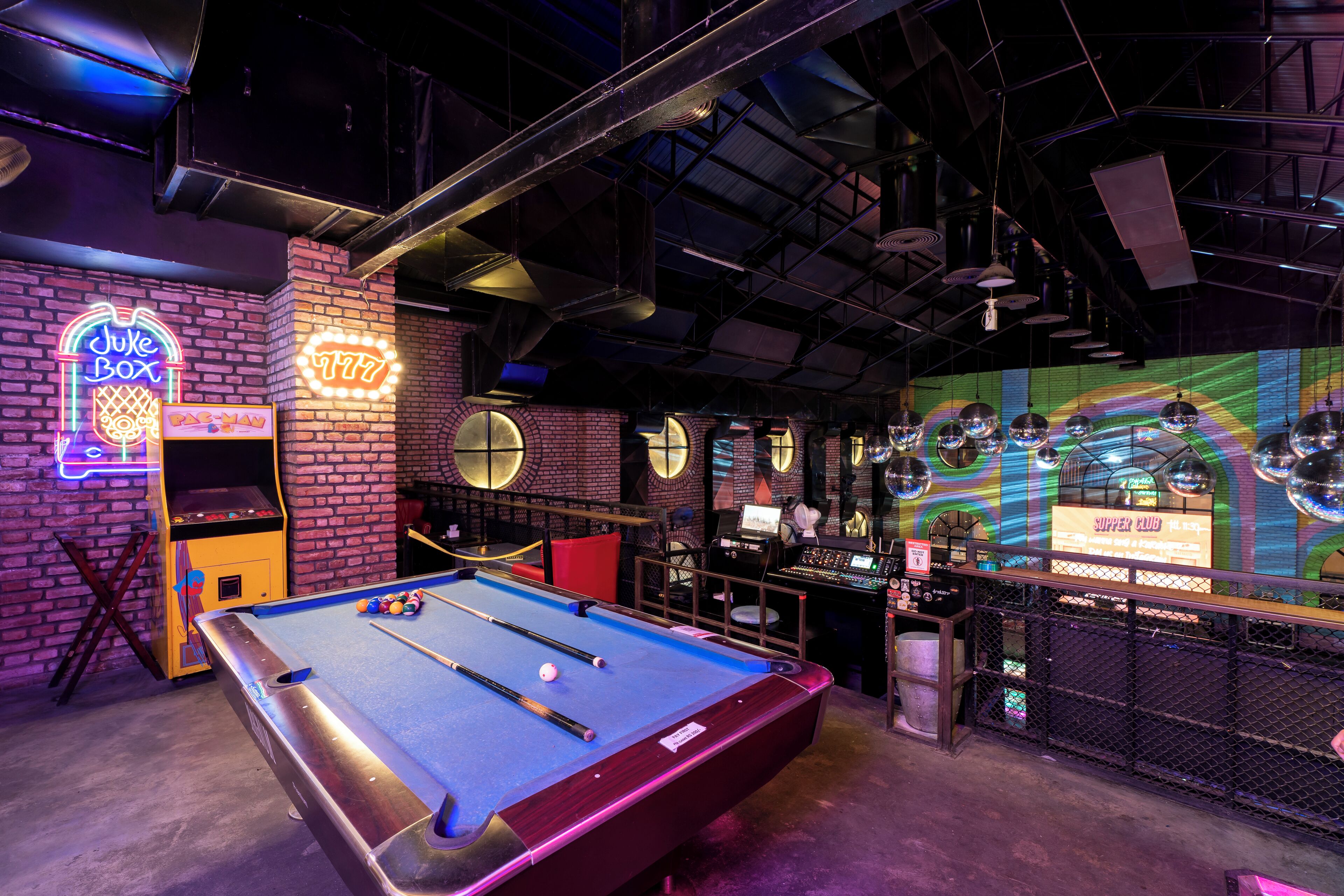 A pool table in a dimly lit room with a brick wall and neon signs.