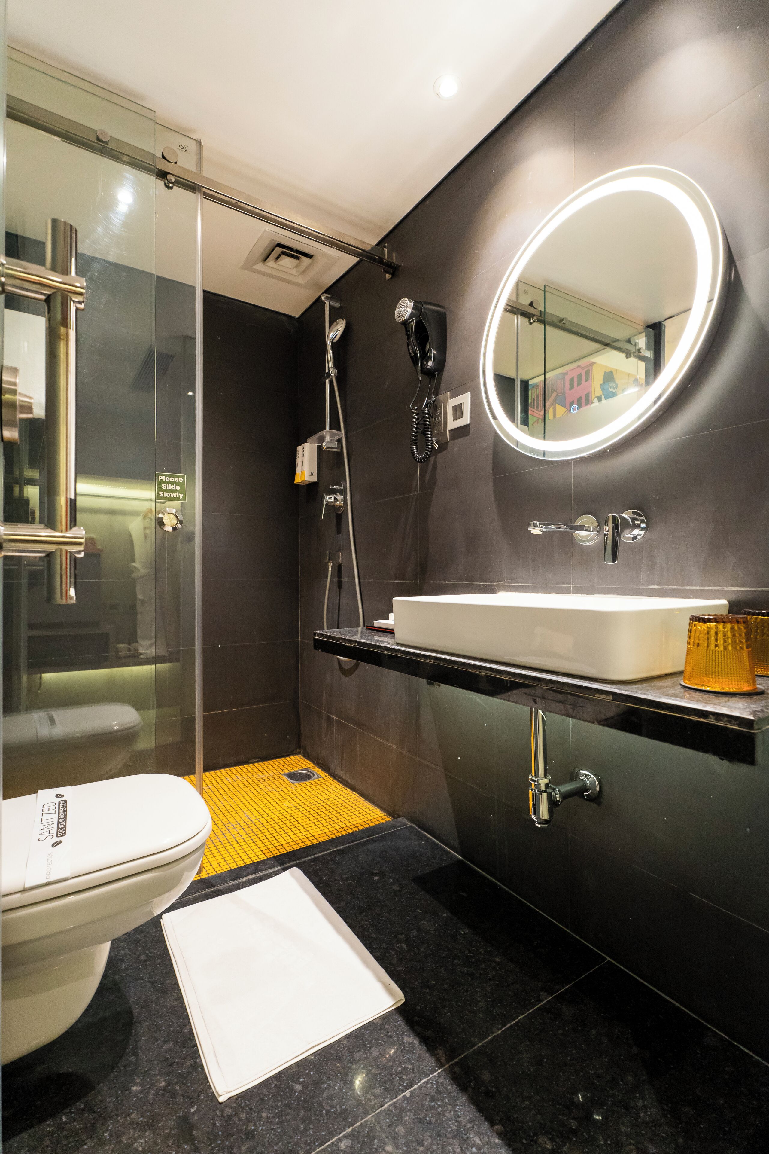 A modern bathroom with a glass-enclosed shower, a white sink, and a mirror with a lighted frame.