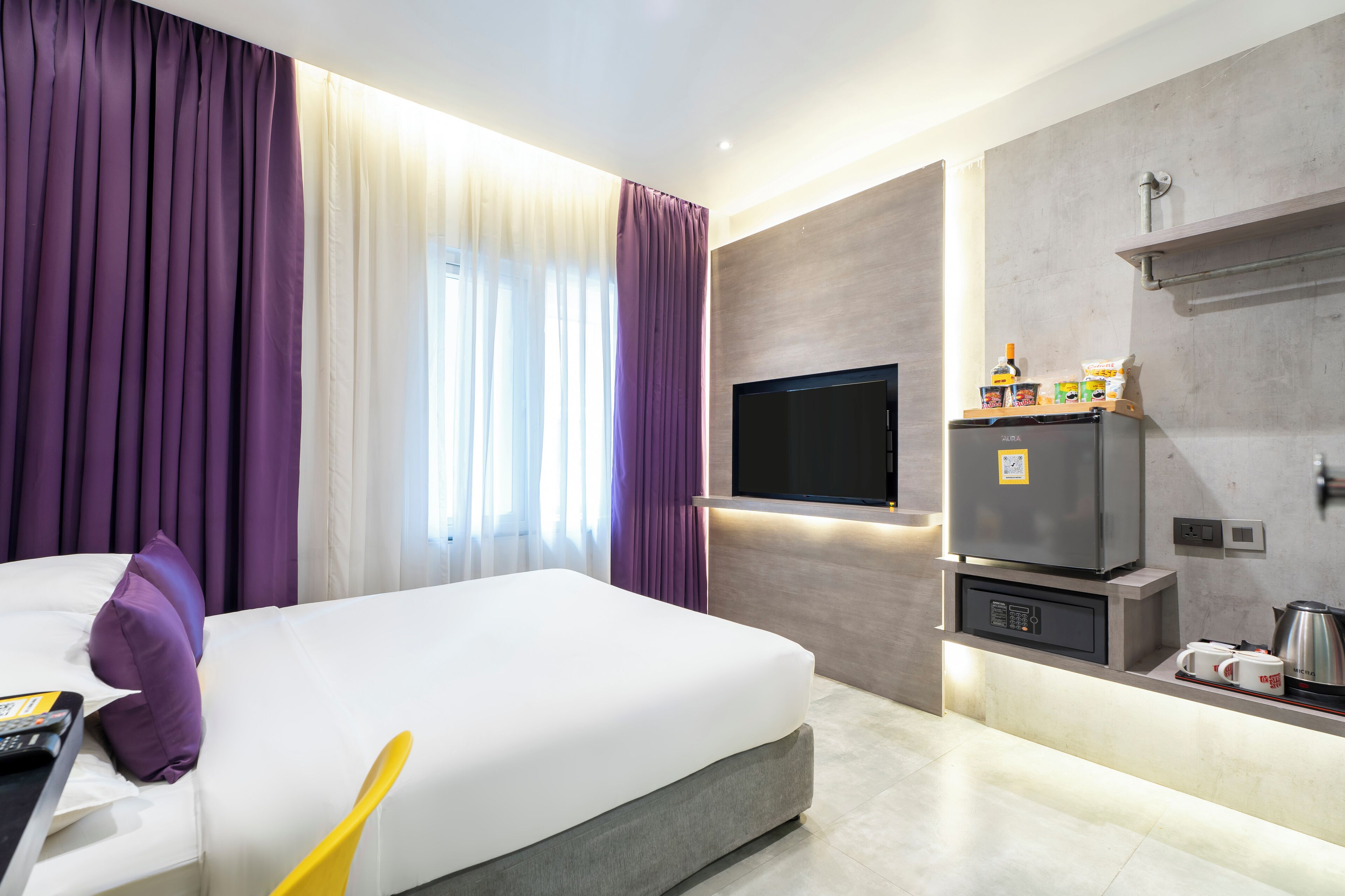 A modern hotel room with a large bed, a flat-screen TV, a minibar, and a built-in coffee machine.