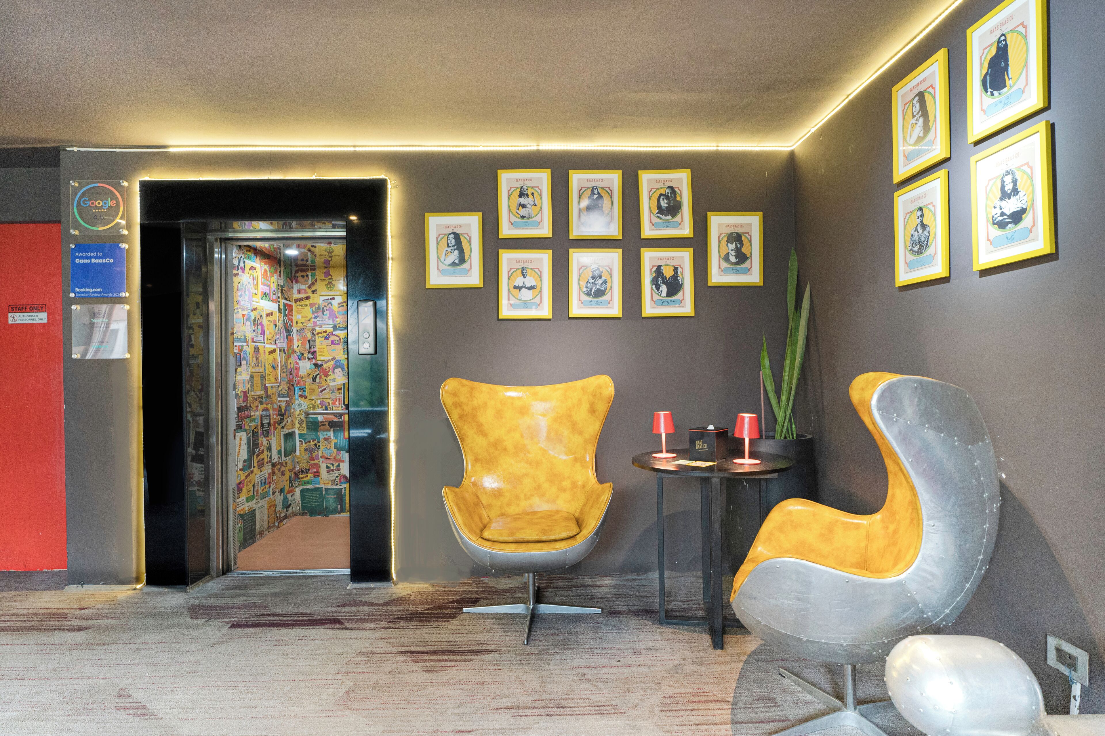 A lobby with two modern chairs, a small table with a red cup, and framed pictures on the wall.
