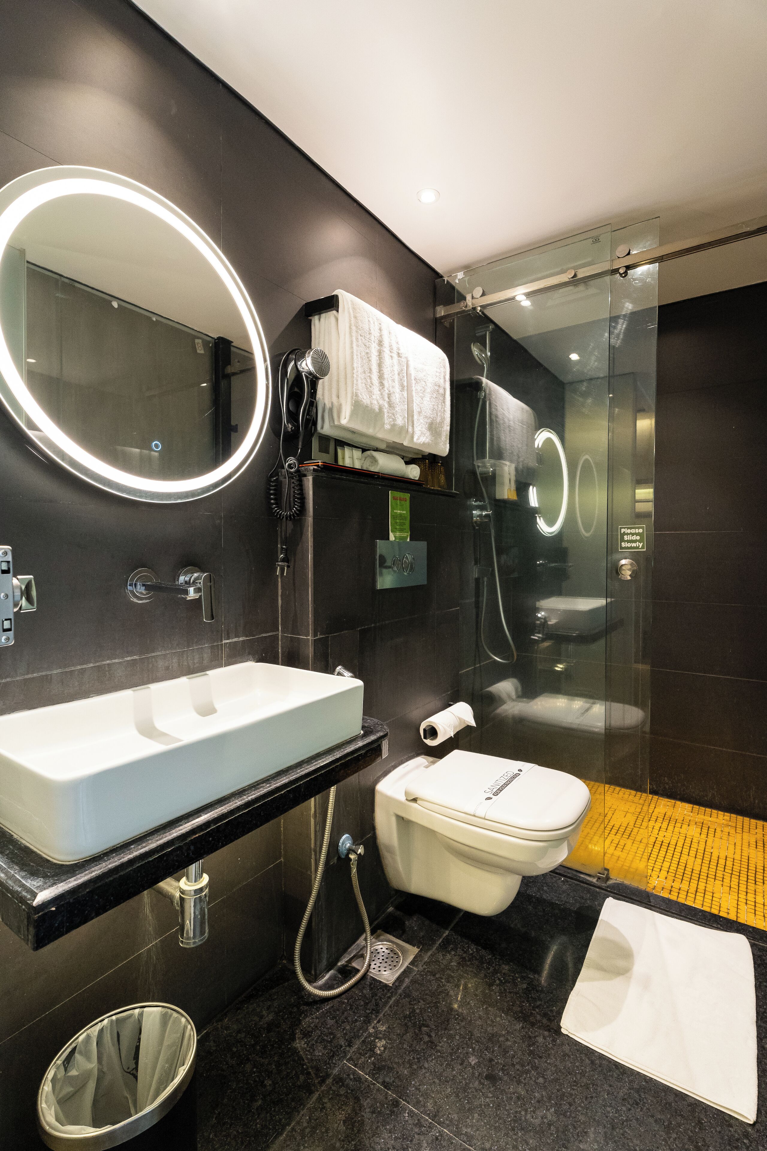 Une salle de bain moderne avec un grand miroir, un lavabo blanc, des toilettes et une douche à parois de verre.