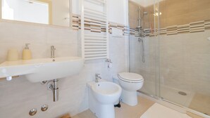 Et moderne badeværelse med et glasafskærmet brusebad, et konsolbord med vask og et toilet.