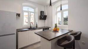 A modern kitchen with a central island, two pendant lights, and a view of the outside through large windows. - Stunning apartment in Split with WiFi (Split)