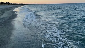 Een strand met golven die zachtjes op de kust komen, een heldere lucht en een verre kustlijn.