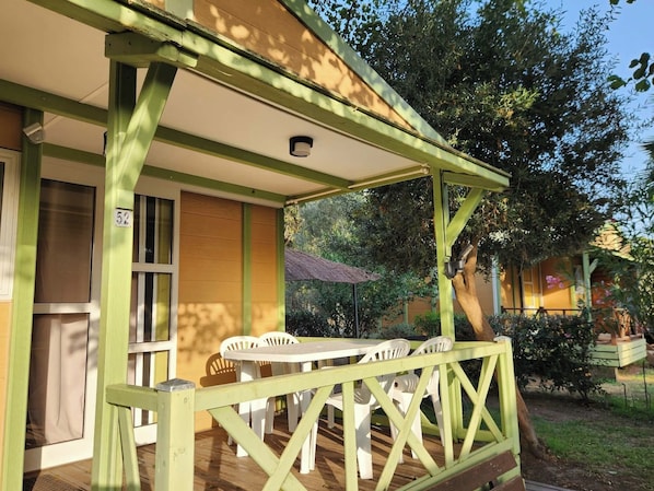 A covered outdoor seating area with a table and chairs, a door, and a window. - Charmant Chalet en Corse 5 Couchages (Sorbo-Ocagnano)