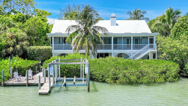 A two-story waterfront house with a balcony, surrounded by lush greenery and a dock. - Sanibel Sunrise - Bayfront home, short walk to the beach! (Sanibel)