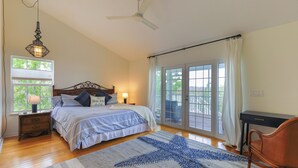 A bedroom with a bed, bedside tables, a desk, a chair, a ceiling fan, and a large window with curtains. - Sanibel Sunrise - Bayfront home, short walk to the beach! (Sanibel)