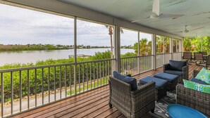 A covered outdoor area with wicker furniture, a view of a lake, and a railing. - Sanibel Sunrise - Bayfront home, short walk to the beach! (Sanibel)
