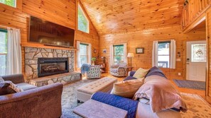 L’intérieur d’une cabane en rondins, avec une cheminée en pierre, des murs en bois et un coin salon confortable.