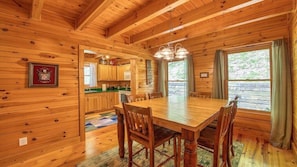 L’intérieur d’un chalet en bois comprend une table à manger, des chaises, un coin cuisine et une grande fenêtre.