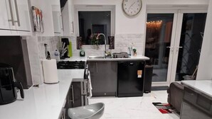 A modern kitchen with a central island, bar stools, and a clock on the wall. - Beautiful and Modern House in Gravesend (Gravesend)
