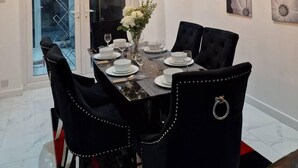 A dining room with a chandelier, white plates, black chairs, and a vase of flowers. - Beautiful and Modern House in Gravesend (Gravesend)