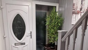 A hallway with a white door, a potted plant, a small table, and a staircase. - Beautiful and Modern House in Gravesend (Gravesend)