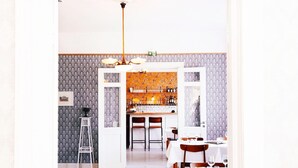 A dining area with a bar in the background, featuring patterned wallpaper and a chandelier. - Carlsro Badhotell (Föglö)