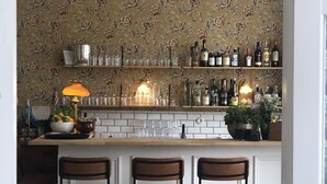 A bar area with three stools, a chandelier, and shelves stocked with bottles and glasses. - Carlsro Badhotell (Föglö)