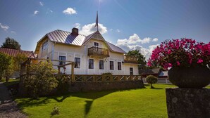 A two-story house with a balcony, a stone wall, and a well-maintained lawn. - Carlsro Badhotell (Föglö)