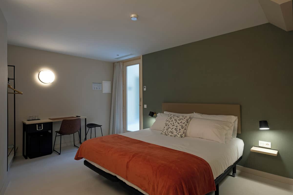 A bedroom with a bed, desk, chair, and a window with curtains.