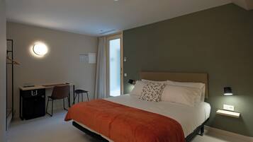 Een slaapkamer met een bed, bureau, stoel en een raam met gordijnen.
