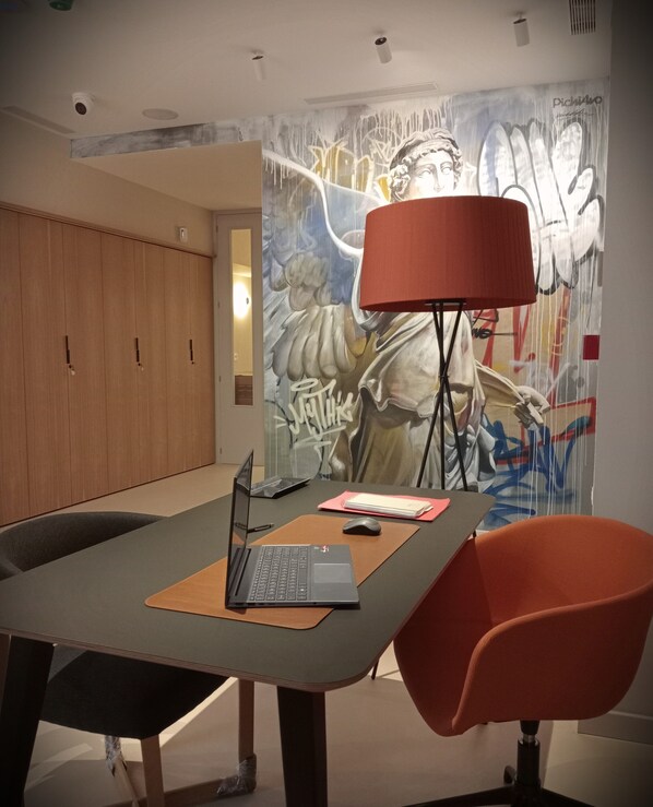 Un salón de conferencias con una computadora portátil sobre una mesa, una lámpara roja y un mural en la pared.