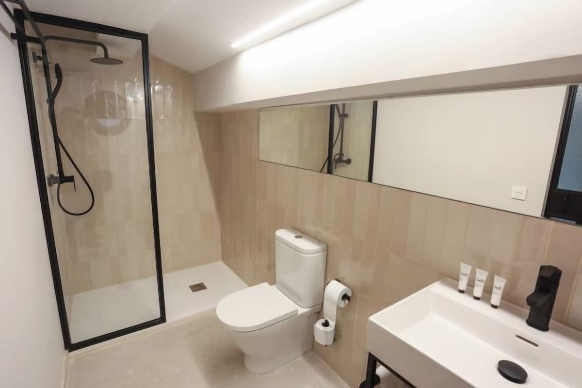 Une salle de bain moderne avec une douche à parois de verre, des toilettes, un lavabo équipé de produits de toilette et un grand miroir.
