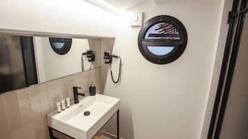 Un baño moderno con lavamanos blanco, grifo negro y un espejo redondo.
