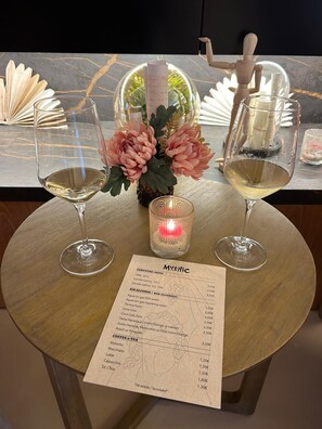 A table with two glasses of white wine, a menu, and a decorative centerpiece with pink flowers. - Mythic Valencia Hotel (Valencia)