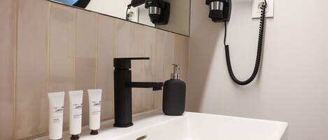 A bathroom with a white sink, black faucet, and three white toiletries.