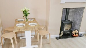 Ein Essbereich mit einem Holztisch, gedeckt für vier Personen, einer Blumenvase und einem Kamin mit Holzscheiten.