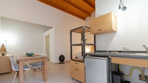 A compact kitchen with a wooden dining table, a built-in refrigerator, and a small sink. - Rosemary - open space in the Hyblean countryside (Sicilia)