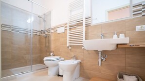 A modern bathroom with a glass shower enclosure, a toilet, a bidet, and a sink with a mirror above. - Rosemary - open space in the Hyblean countryside (Sicilia)