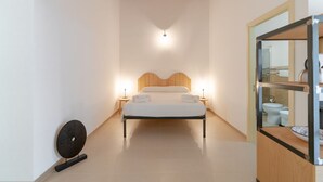 A bedroom with a bed, bedside lamps, a wall-mounted fan, and a bathroom visible through a glass door. - Rosemary - open space in the Hyblean countryside (Sicilia)