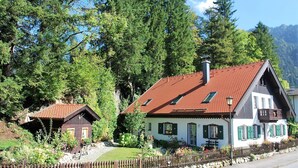 Un edificio in stile chalet tradizionale con tetto in tegole rosse, immerso nel verde e circondato da un muretto in pietra.